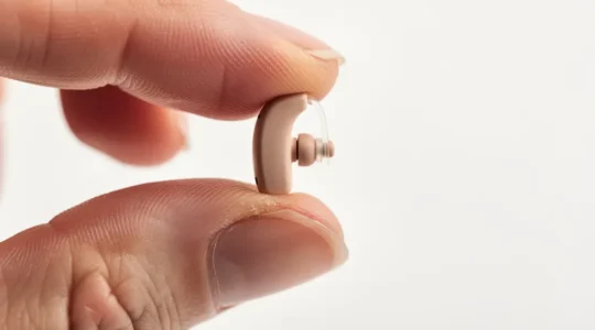 Main tenant délicatement un appareil auditif intra-auriculaire invisible entre le pouce et l'index