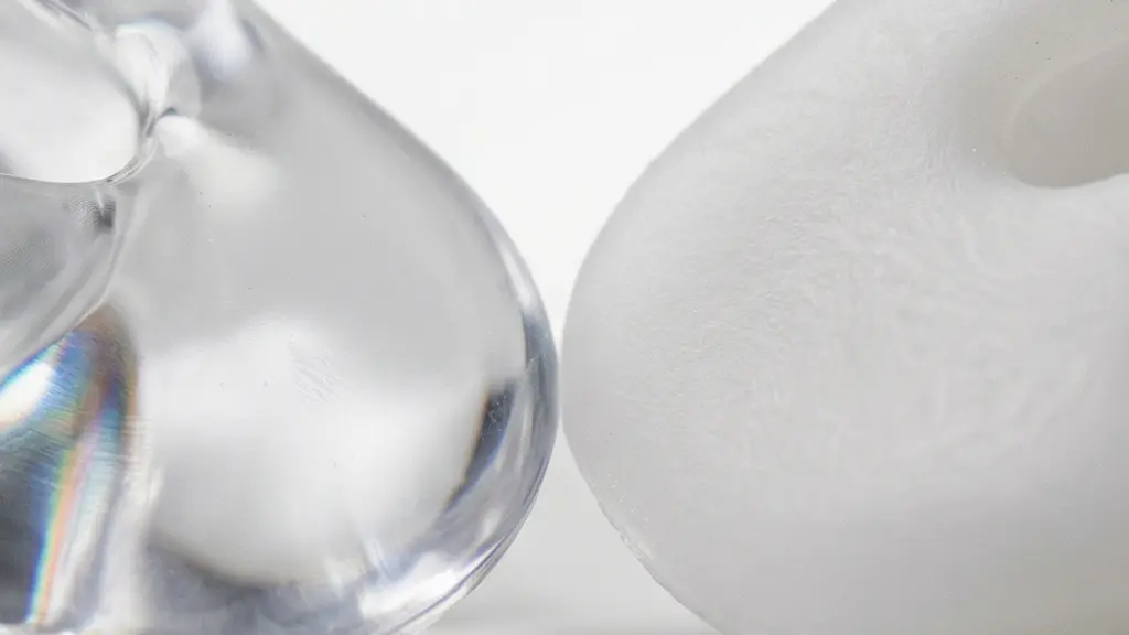 Vue macro extrême de la surface texturée d'un embout auditif en acrylique translucide à côté d'un embout en silicone souple, révélant les différences de finition et de matière.