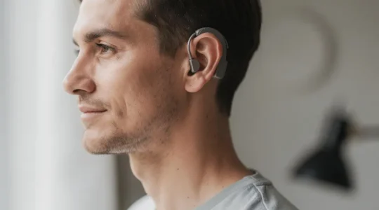 Portrait éditorial réaliste d’une personne portant une aide auditive micro-contour RIC derrière l’oreille, avec un grand espace négatif pour une mise en page.